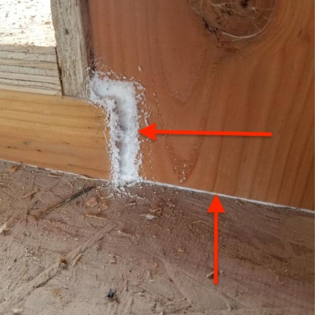 Close-up of a wood corner joint with white sealant or foam, marked by red arrows.