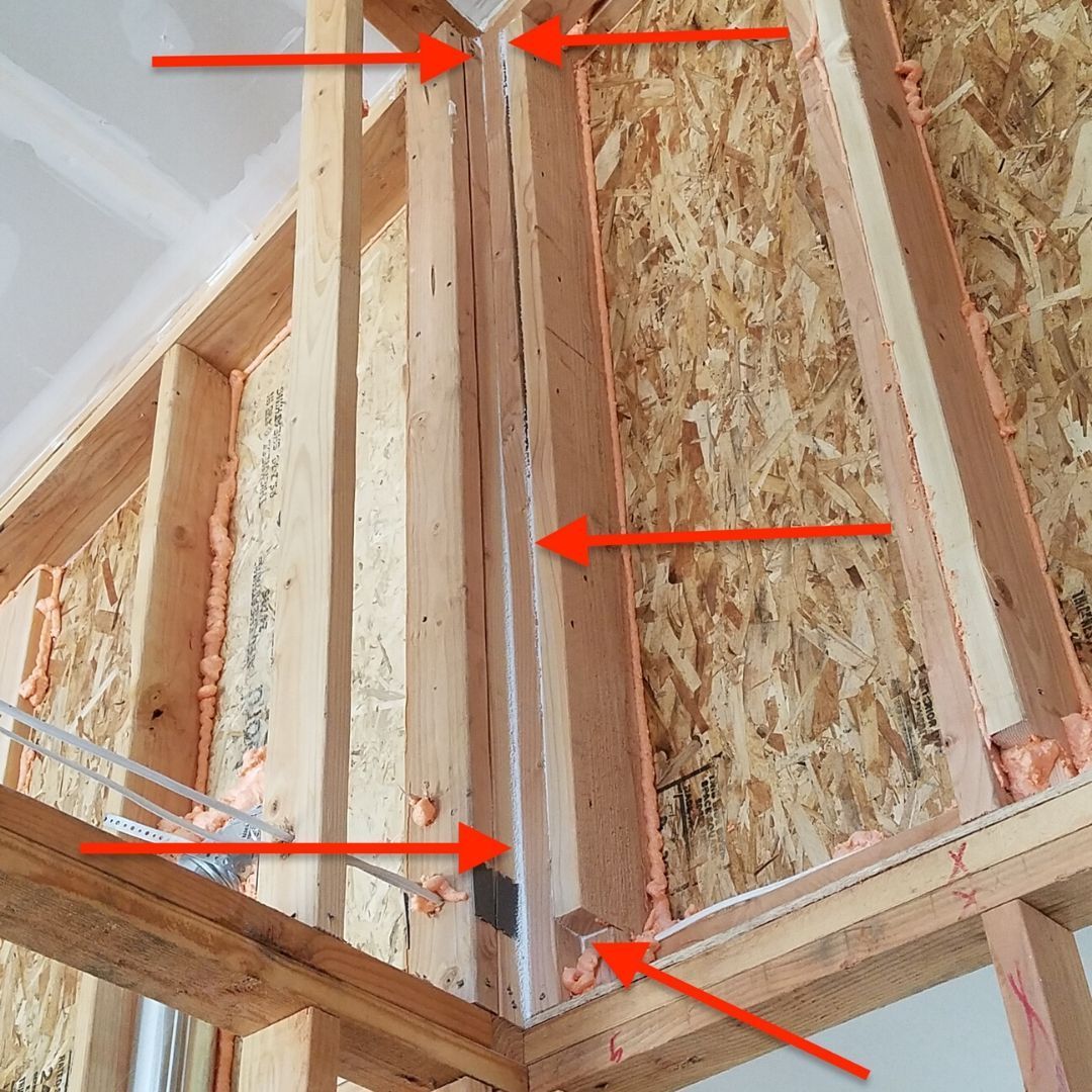 Framed wall corner with exposed wood studs and arrows pointing to structural points.