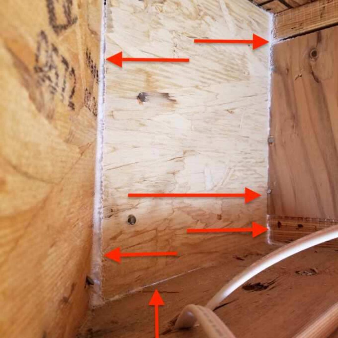 Arrows pointing to gaps in a plywood corner joint inside a wooden structure