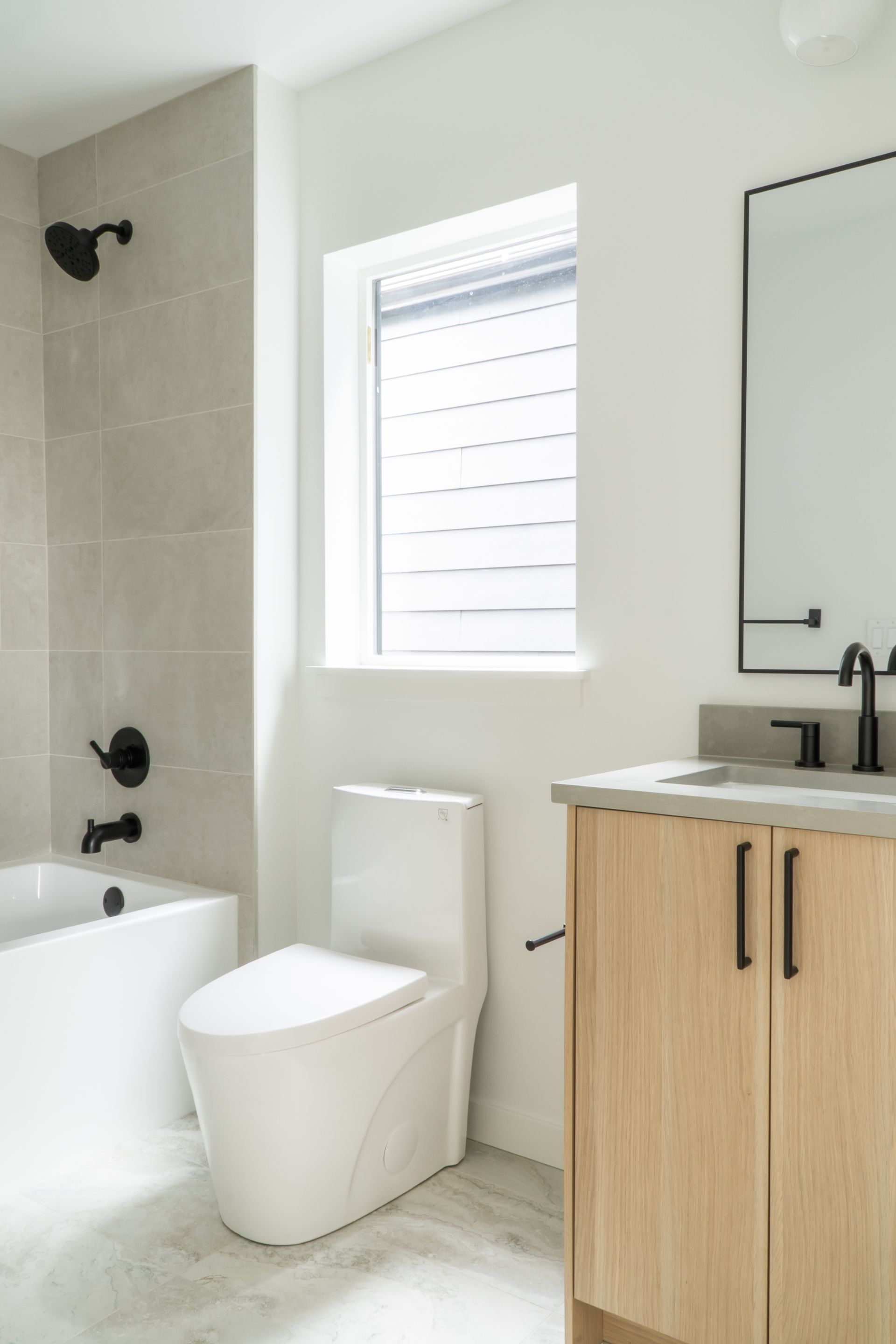 Modern bathroom with bathtub, toilet, window, and wood vanity.