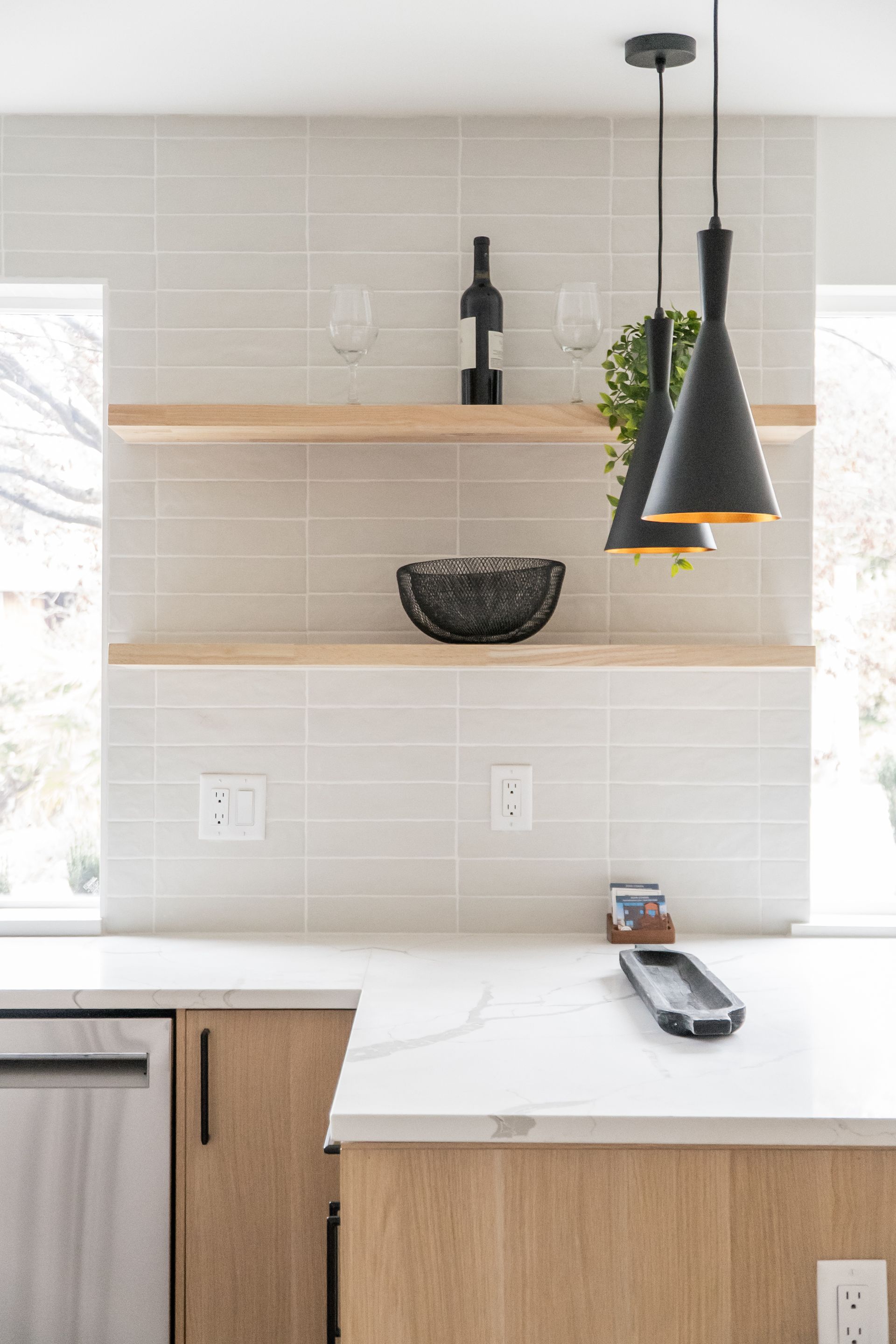 Modern kitchen with light wood cabinets, floating shelves, pendant lights, and a white countertop.