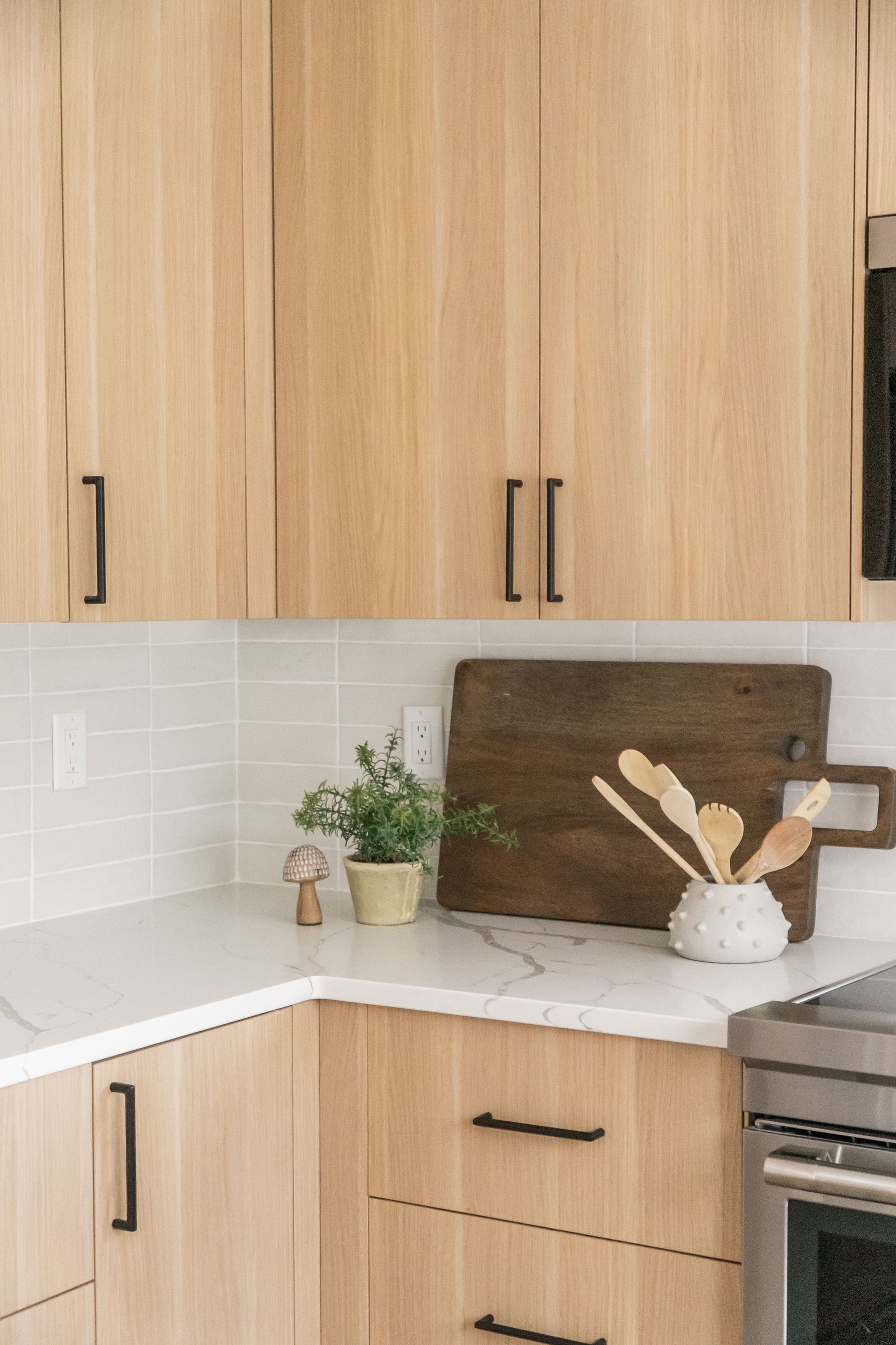Bright kitchen corner with wood cabinets, white tile backsplash, marble counter, and decorative plants and utensils