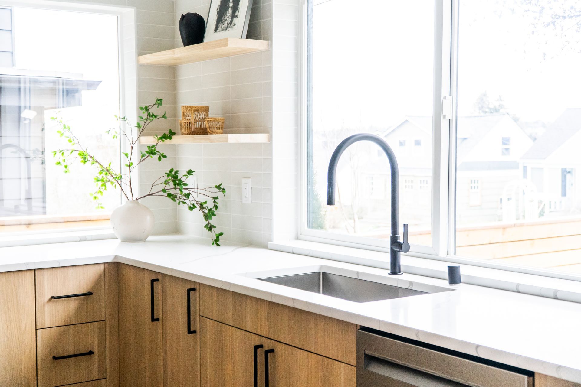 Bright kitchen sink area with wood cabinets, white countertops, and a vase by the window