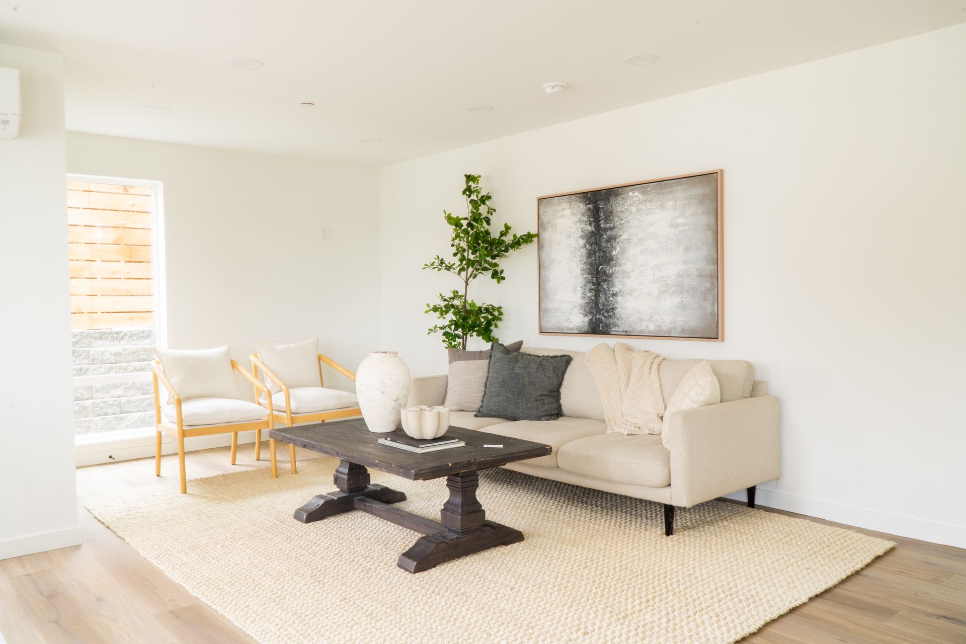 Bright minimalist living room with cream sofa, black coffee table, abstract wall art, and white rug