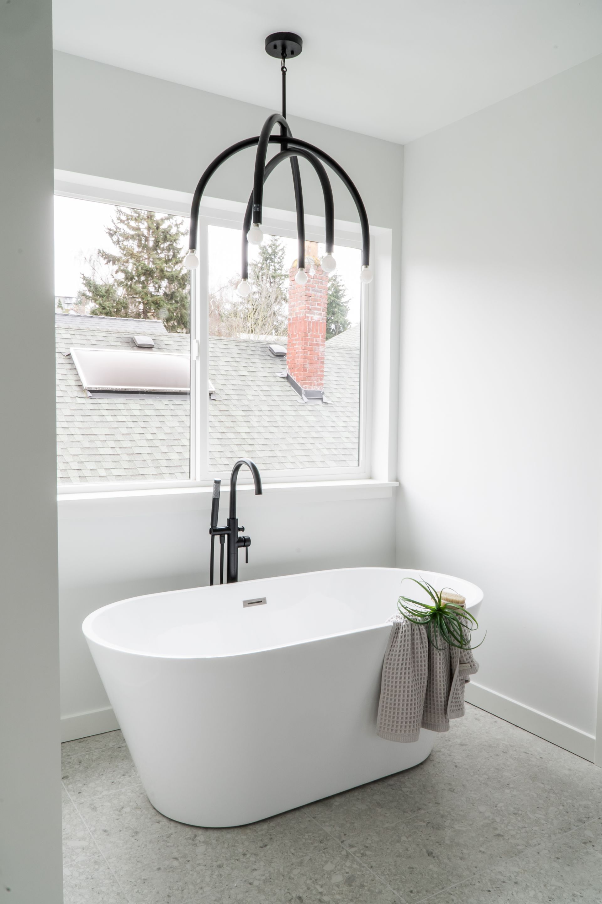 Modern bathroom with freestanding white tub, black faucet, and large window overlooking snow outside