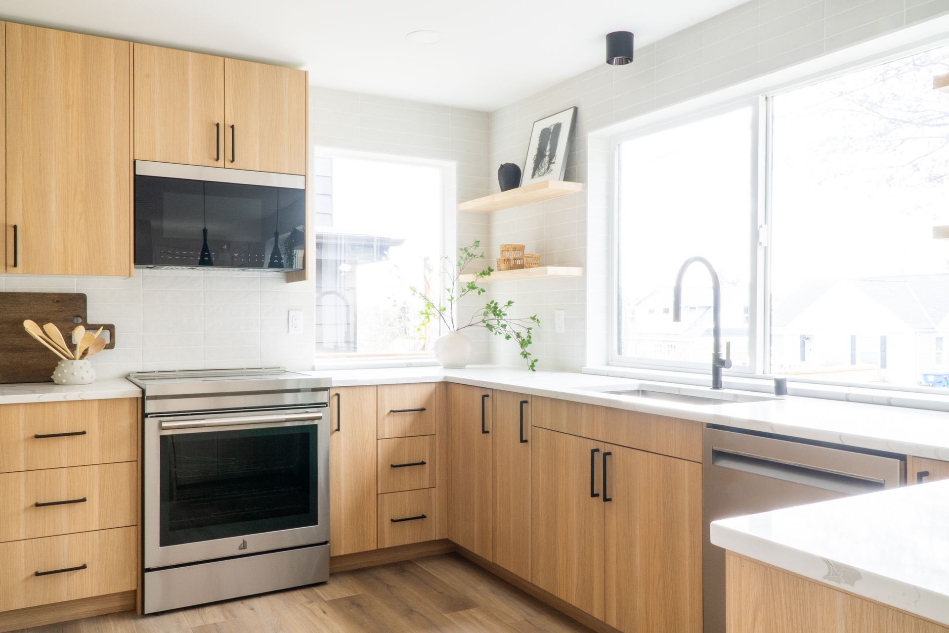 Bright modern kitchen with wood cabinets, stainless stove, white counters, and a sunlit sink window