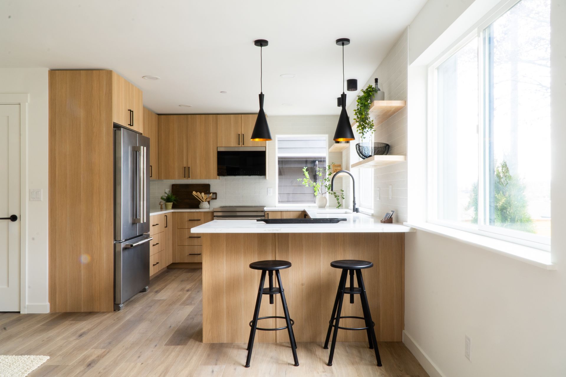 Bright modern kitchen with wood cabinets, marble island, black stools, and large window.