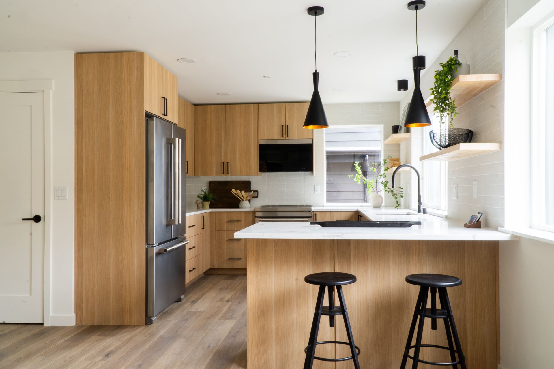 Modern kitchen with wood cabinets, white island, stainless fridge, and two black stools