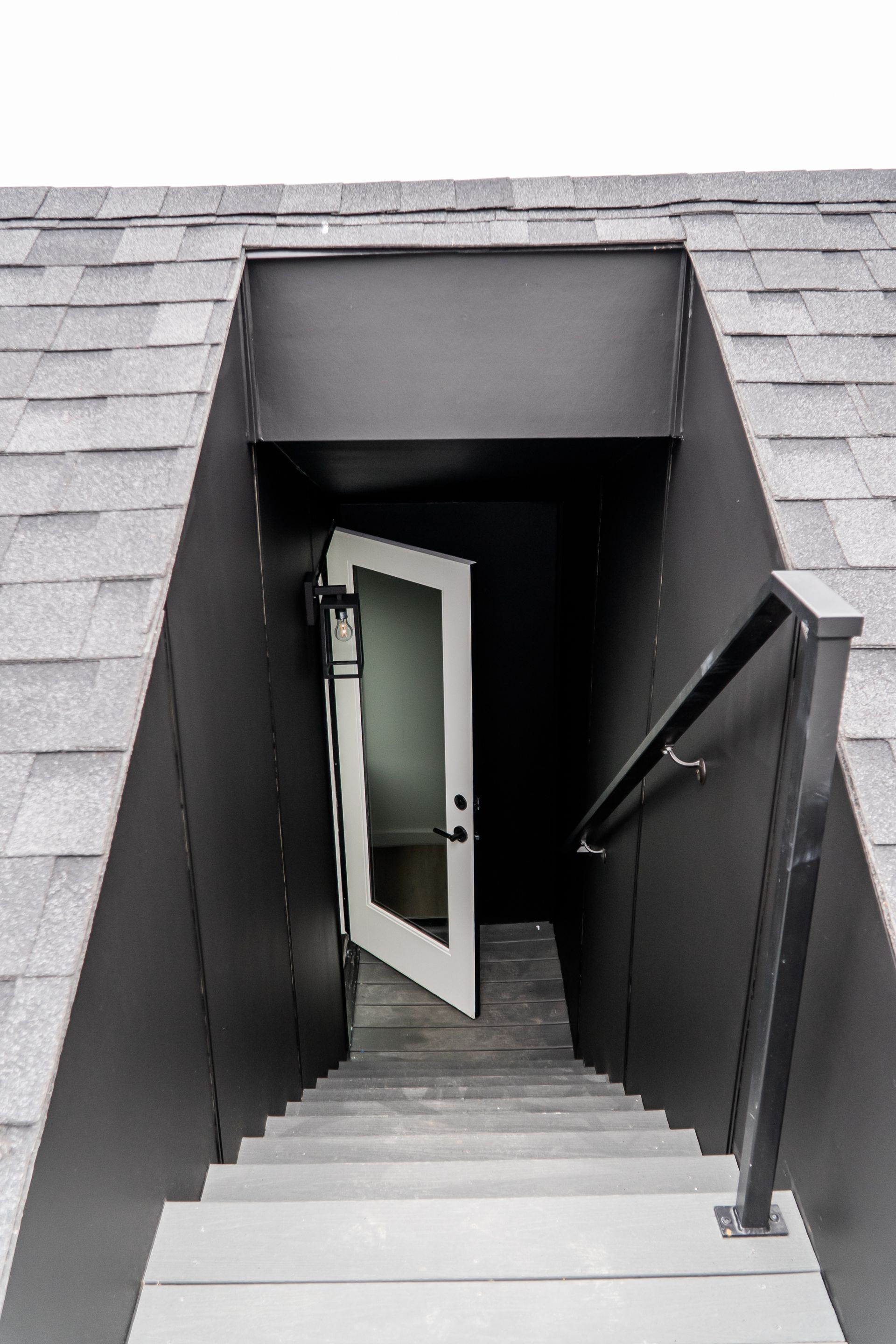 Narrow stairwell leading to an open white door beneath a gray shingled roof.