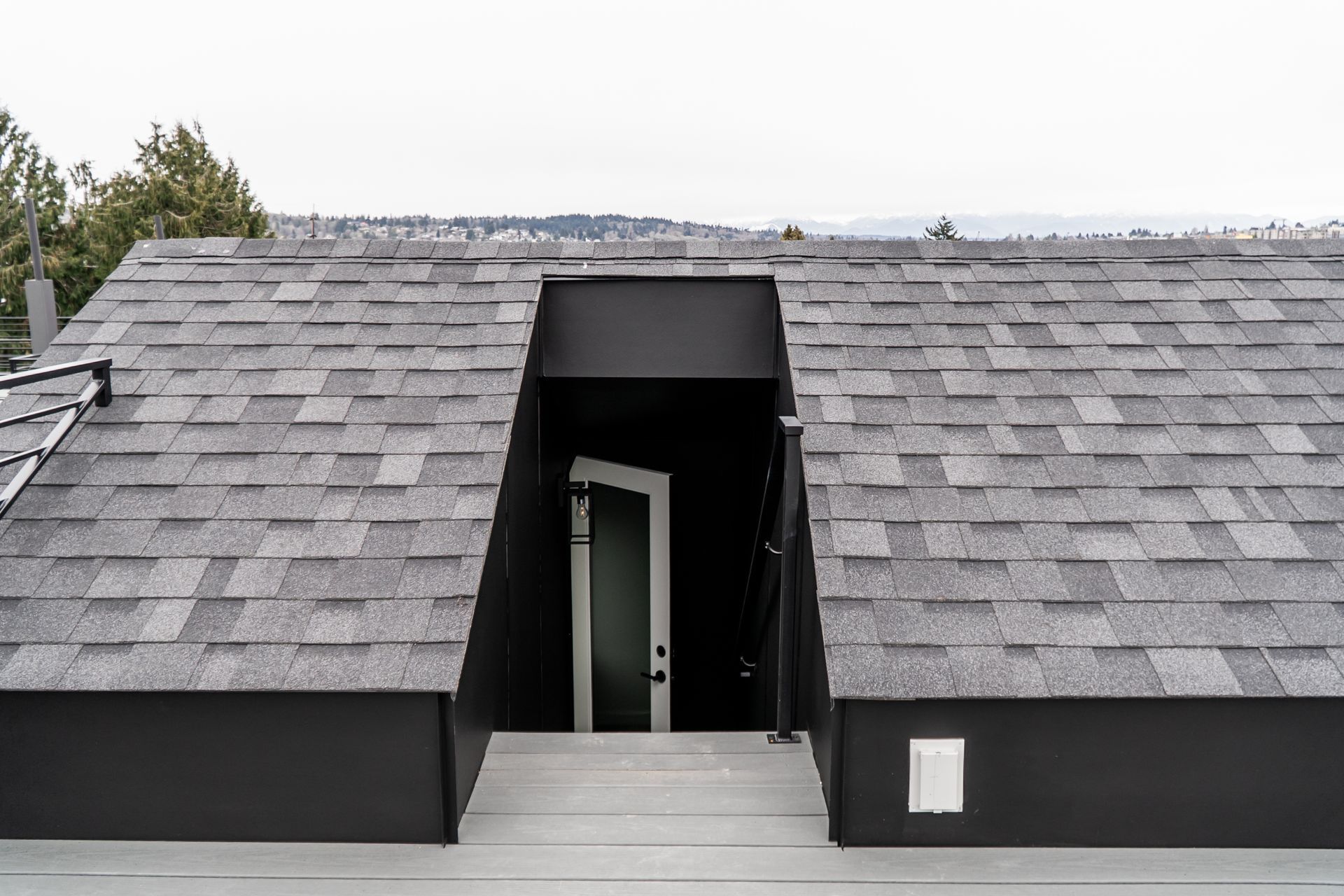 Modern rooftop with gray shingles and a centered dark dormer opening above a skylight-like entrance.