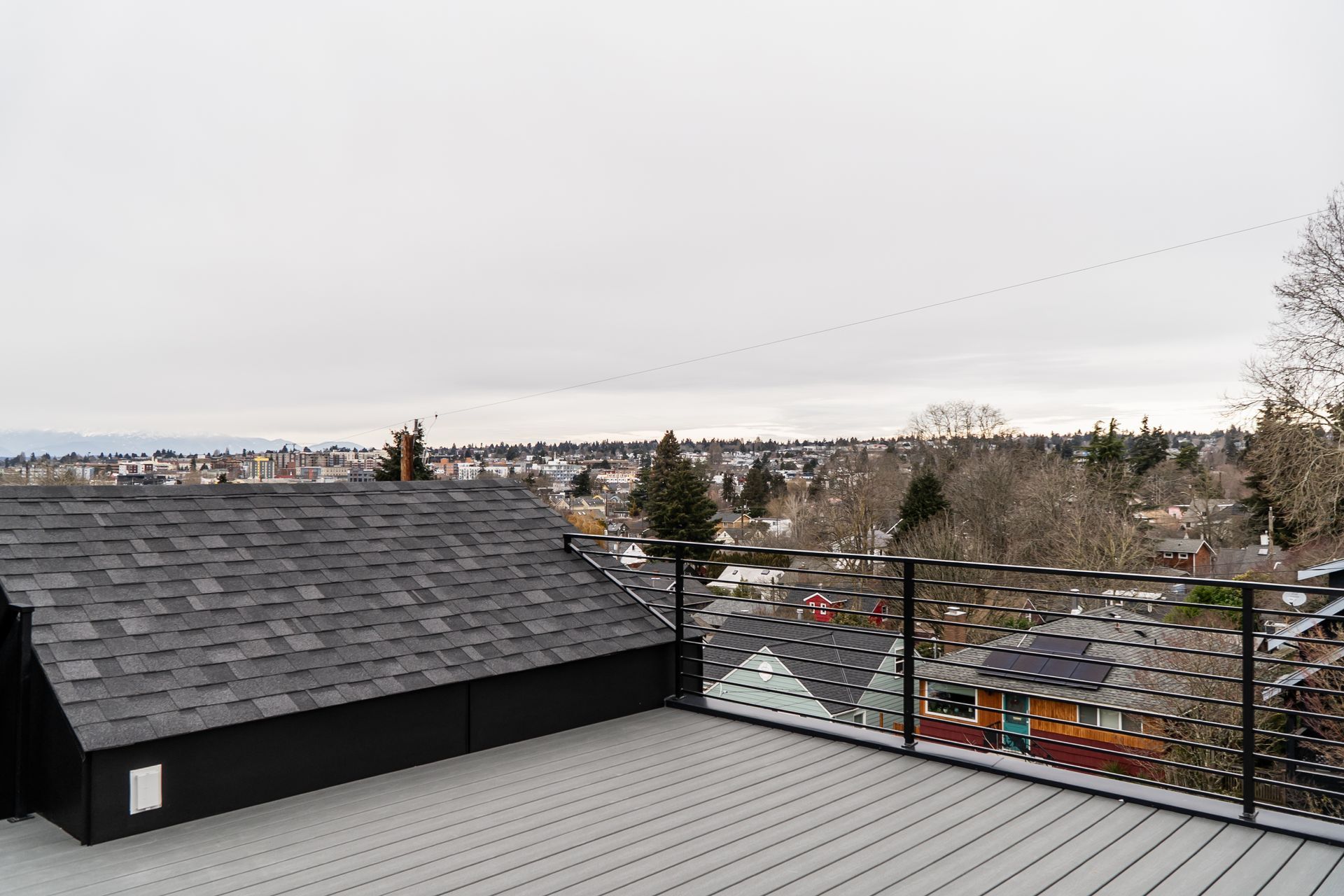 Rooftop view of a gray suburban neighborhood under an overcast sky, with trees and distant houses.