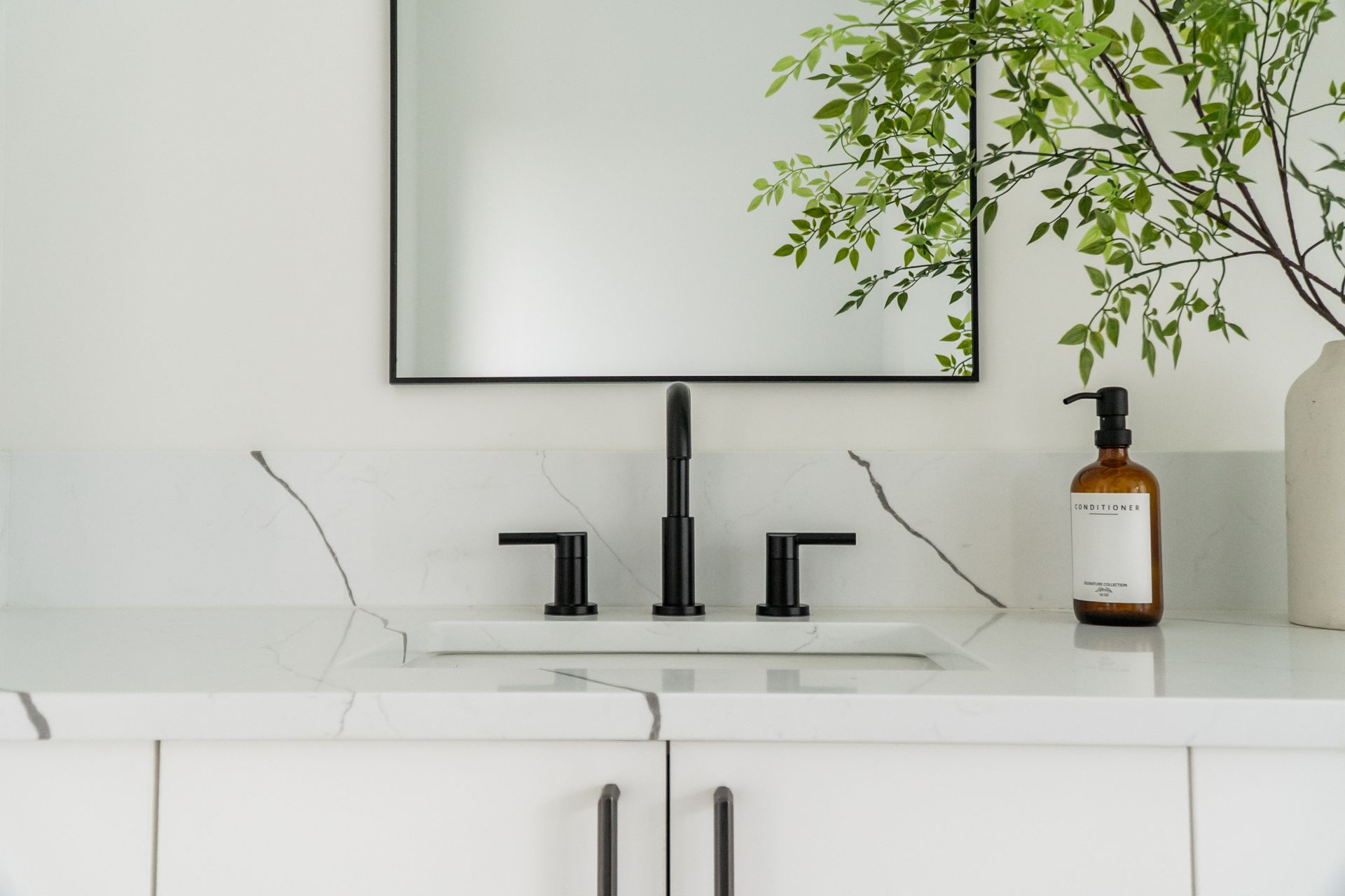 Minimalist bathroom vanity with black faucet, white countertop, mirror, and amber soap dispenser