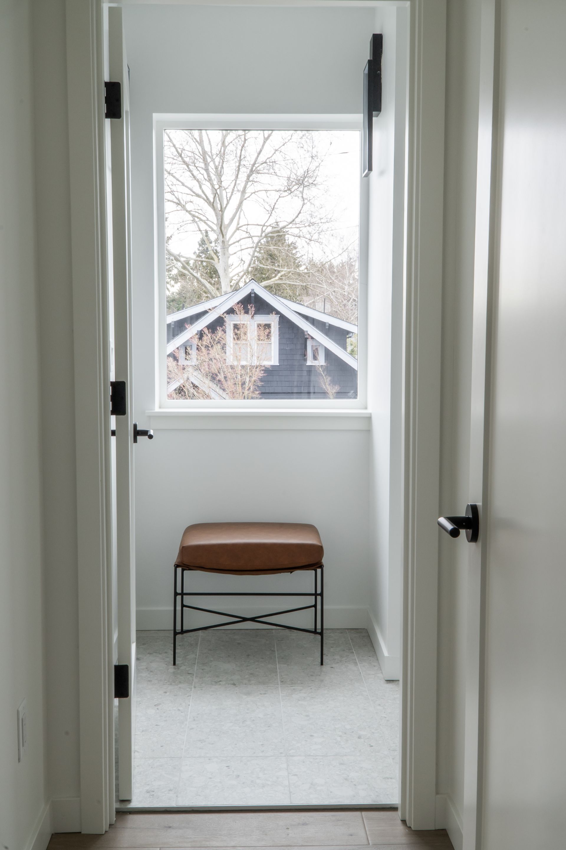 Narrow hallway view through a door to a small stool by a window overlooking snowy rooftops.