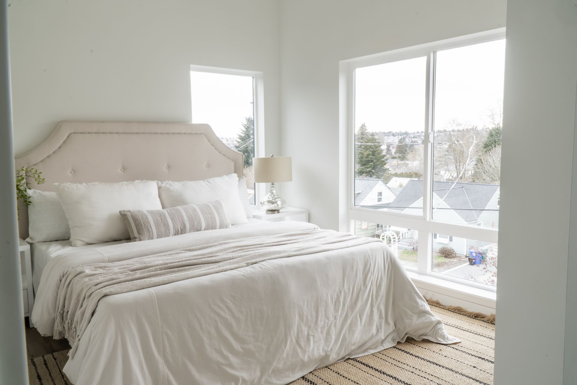 Bright bedroom with a white bed, beige headboard, and large windows overlooking a snowy view.