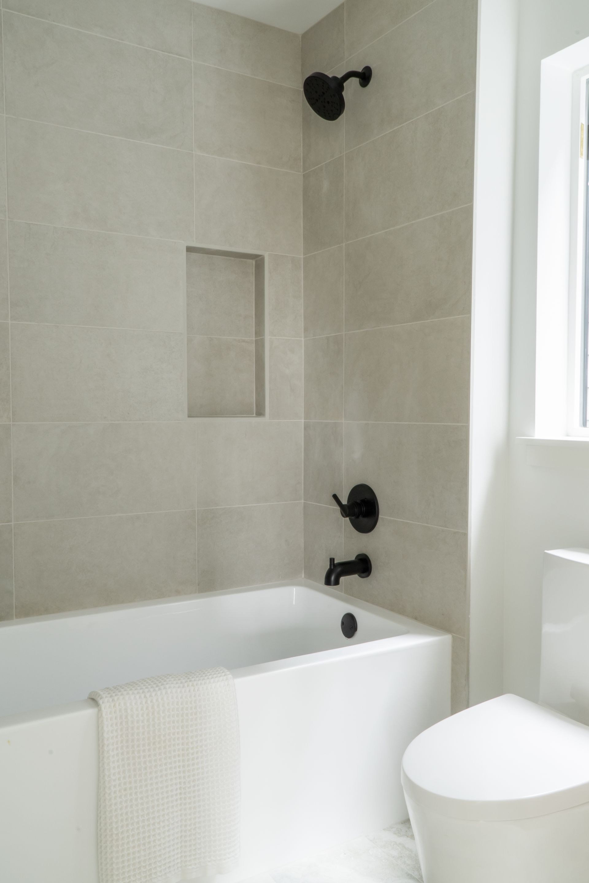 Modern bathroom with tiled shower, built-in niche, black fixtures, and a white tub beside a toilet