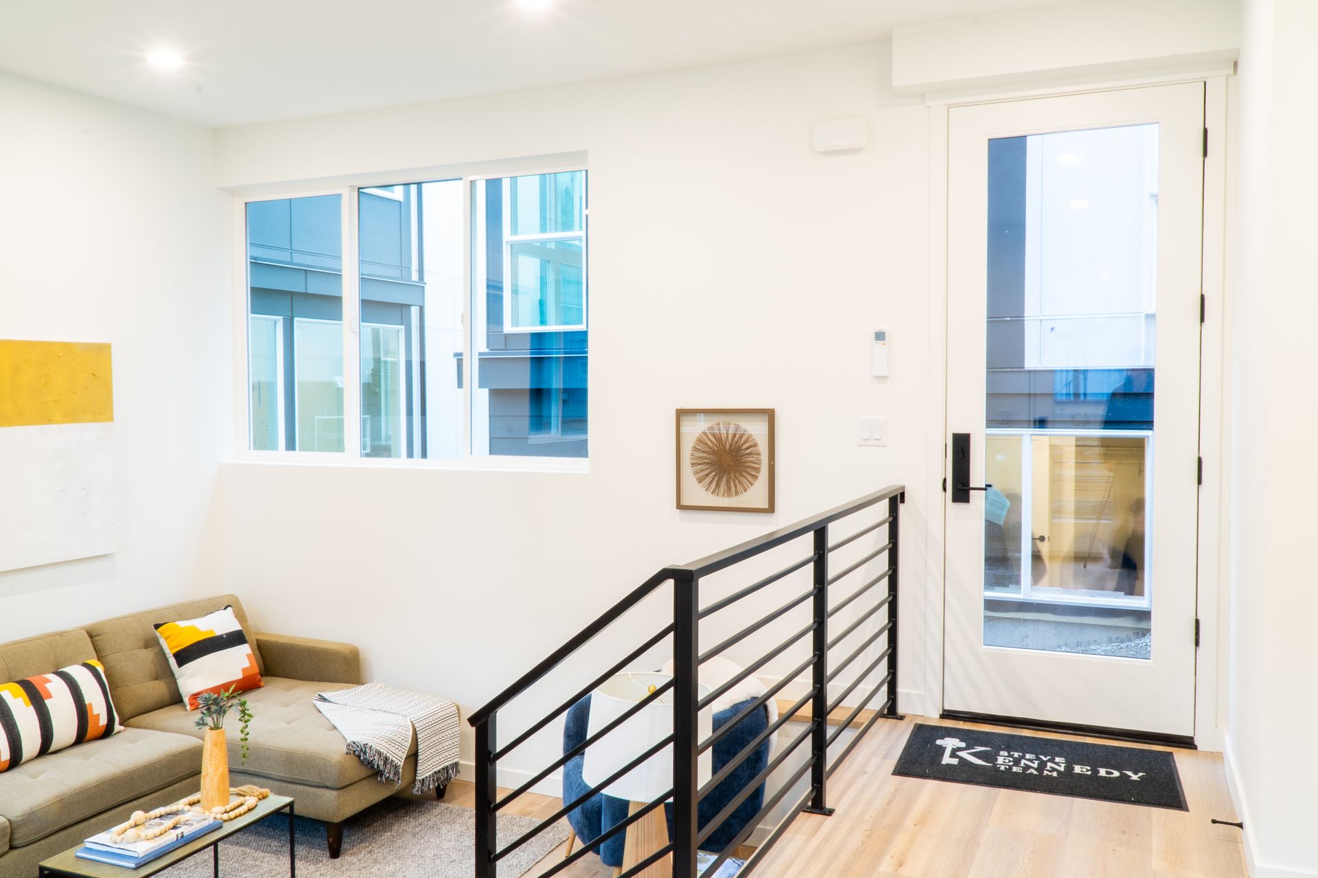 Bright modern stair landing with black railing, sofa, windows, and balcony door