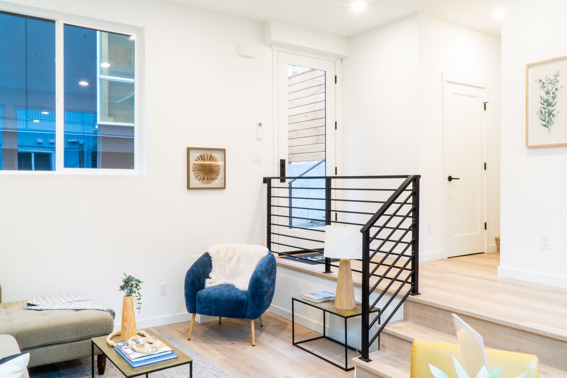 Bright modern living room with blue chair, white sofa, black railing, and large window