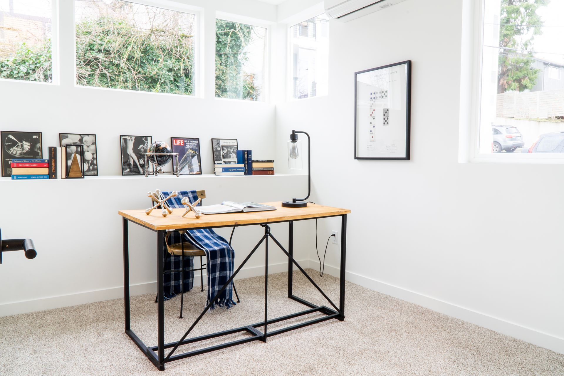 Bright home office with a desk, laptop, books, and large windows