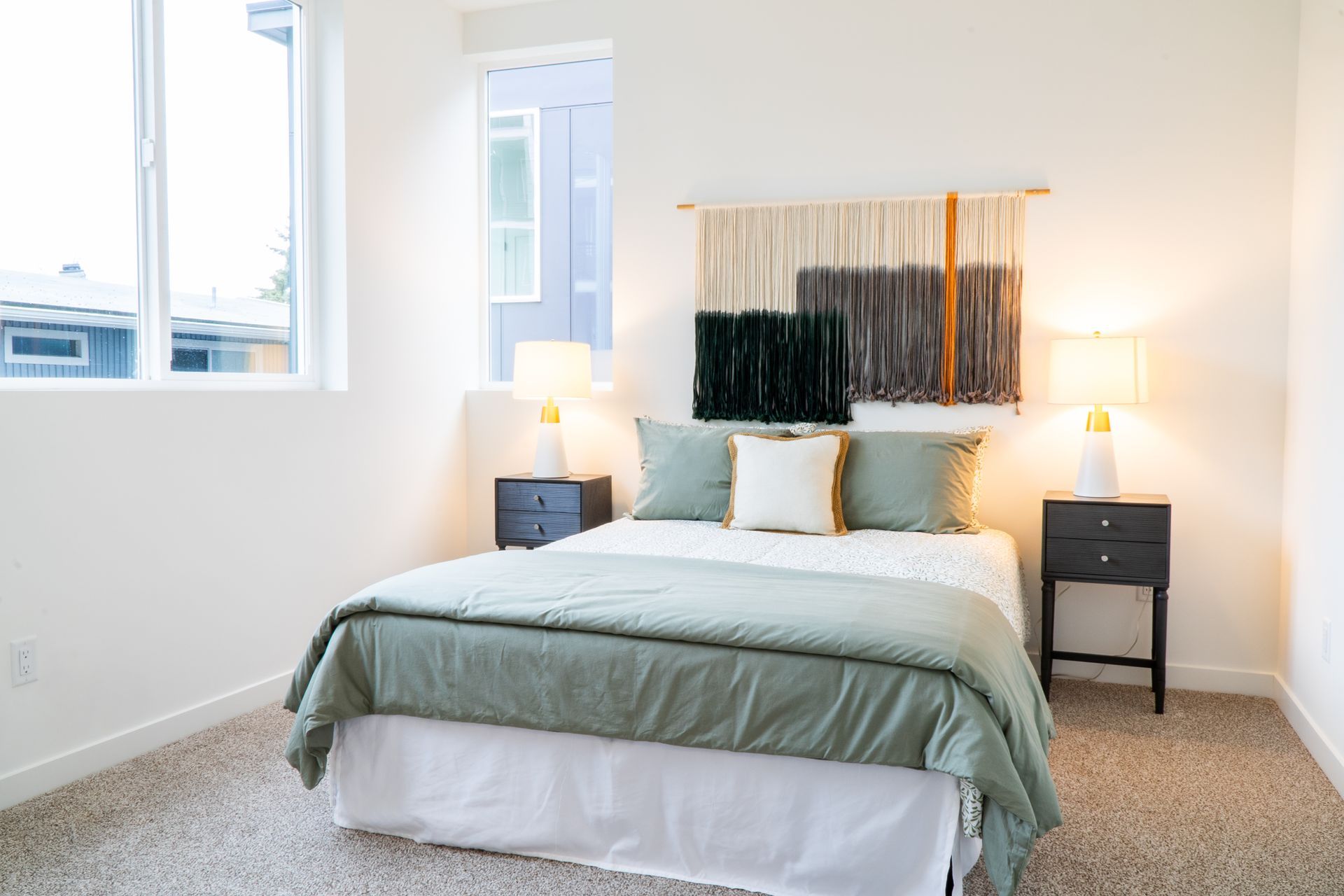 Bright bedroom with a made bed, bedside lamps, wall art, and a window letting in daylight