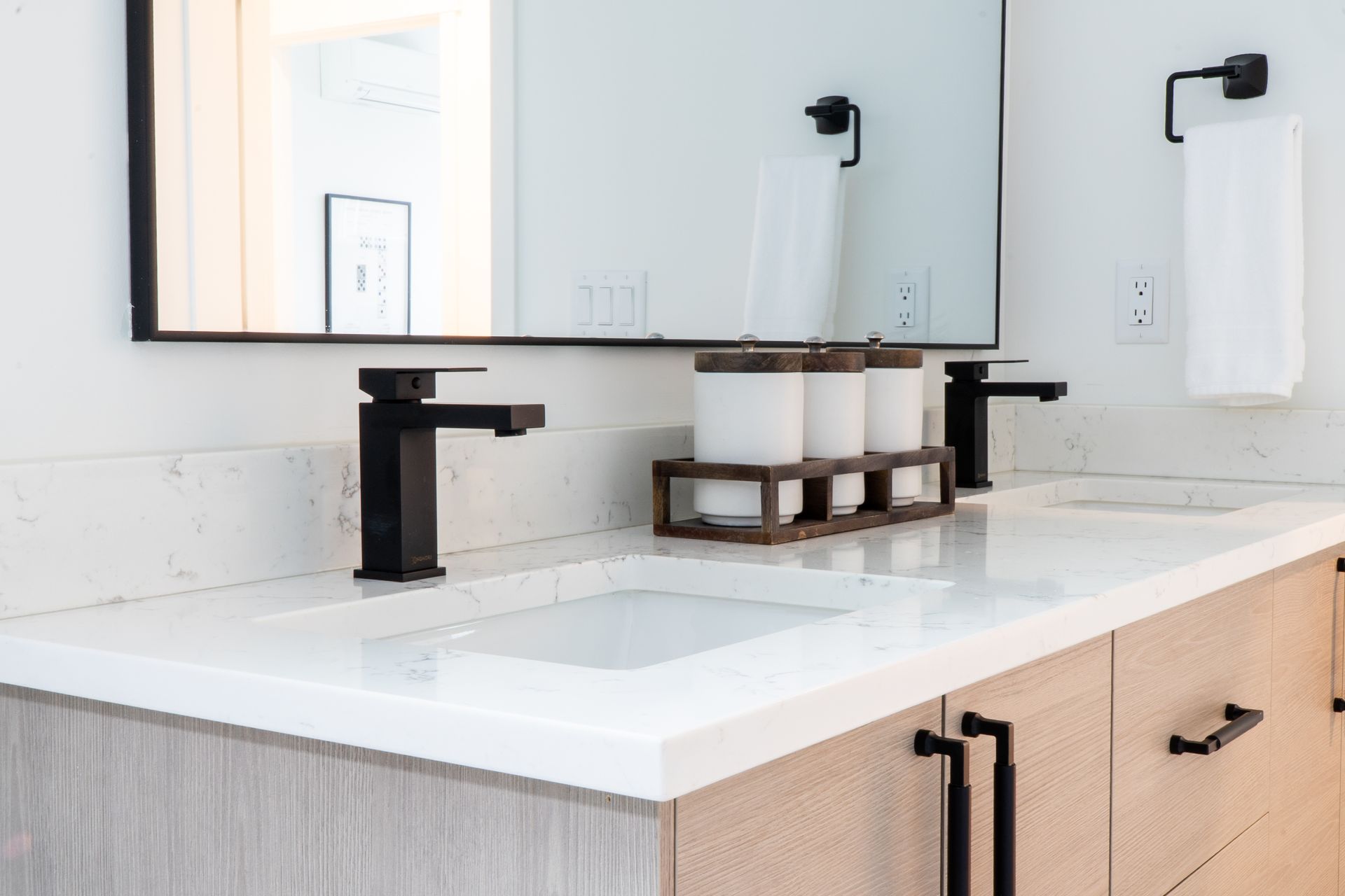 Modern bathroom vanity with a double sink, black faucets, and a large mirror above a light wood cabinet.
