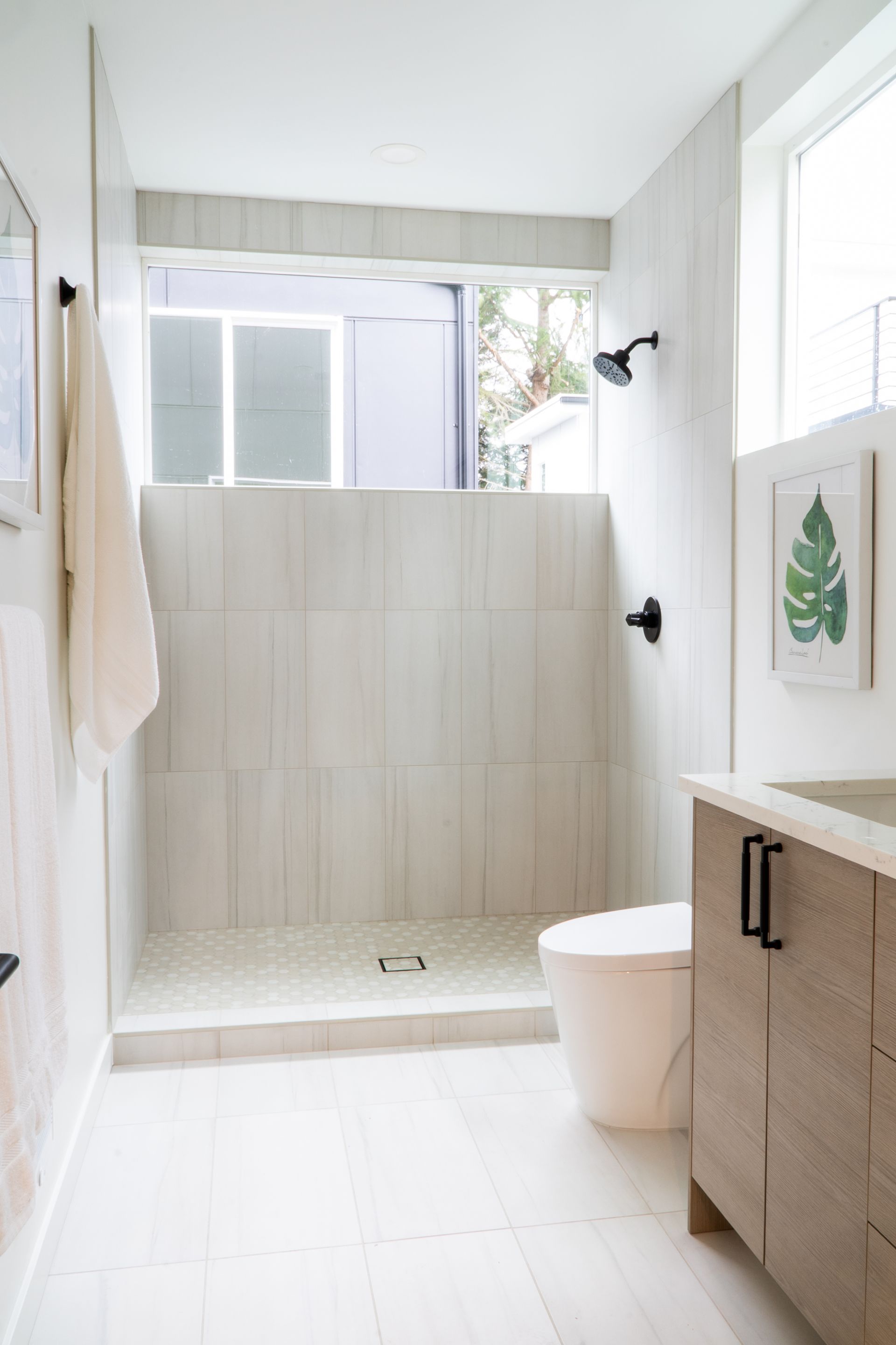 Bright bathroom with white walk-in shower, tiled walls, toilet, and wood vanity