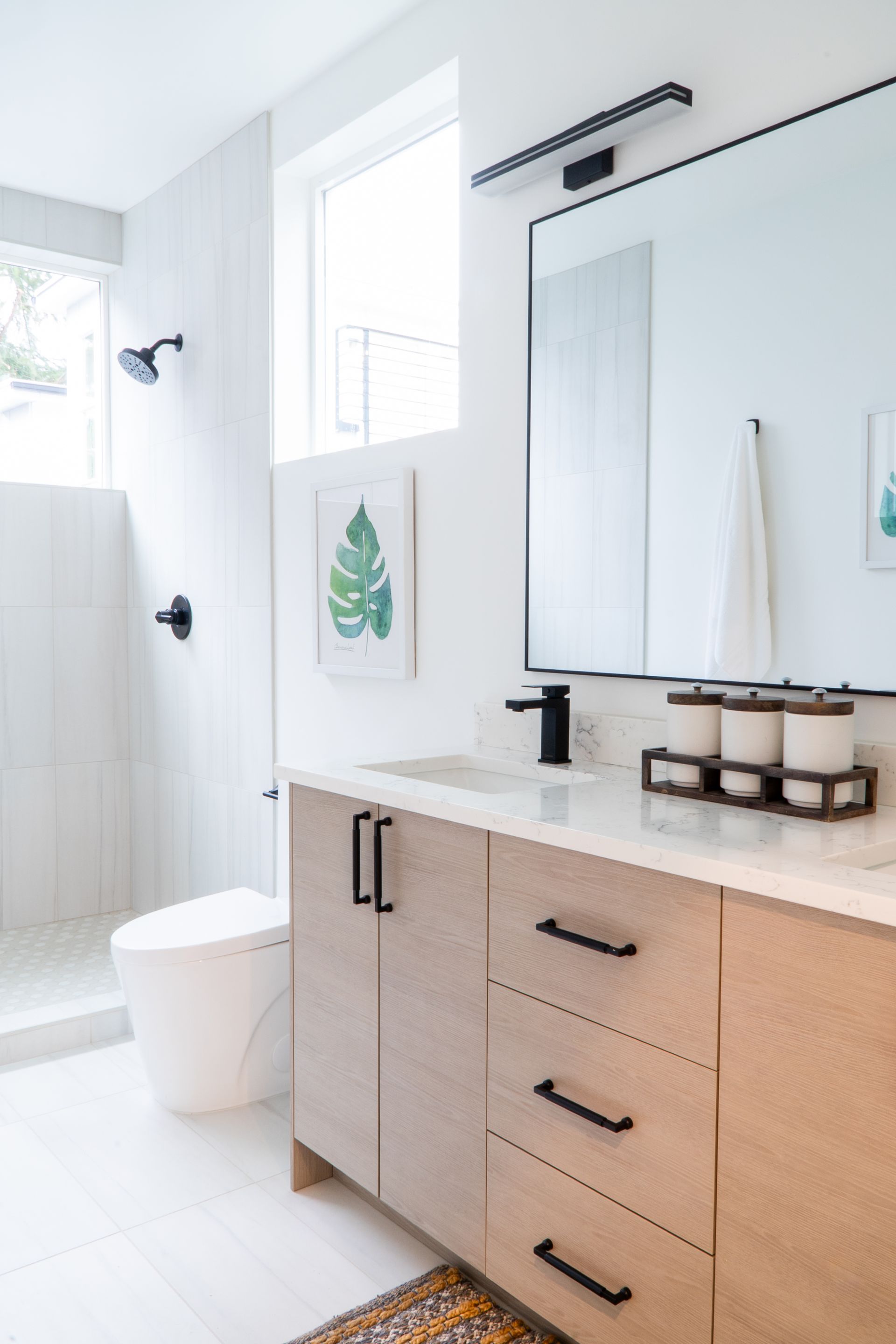 Bright bathroom with white shower, vanity, large mirror, and toiletries on a counter