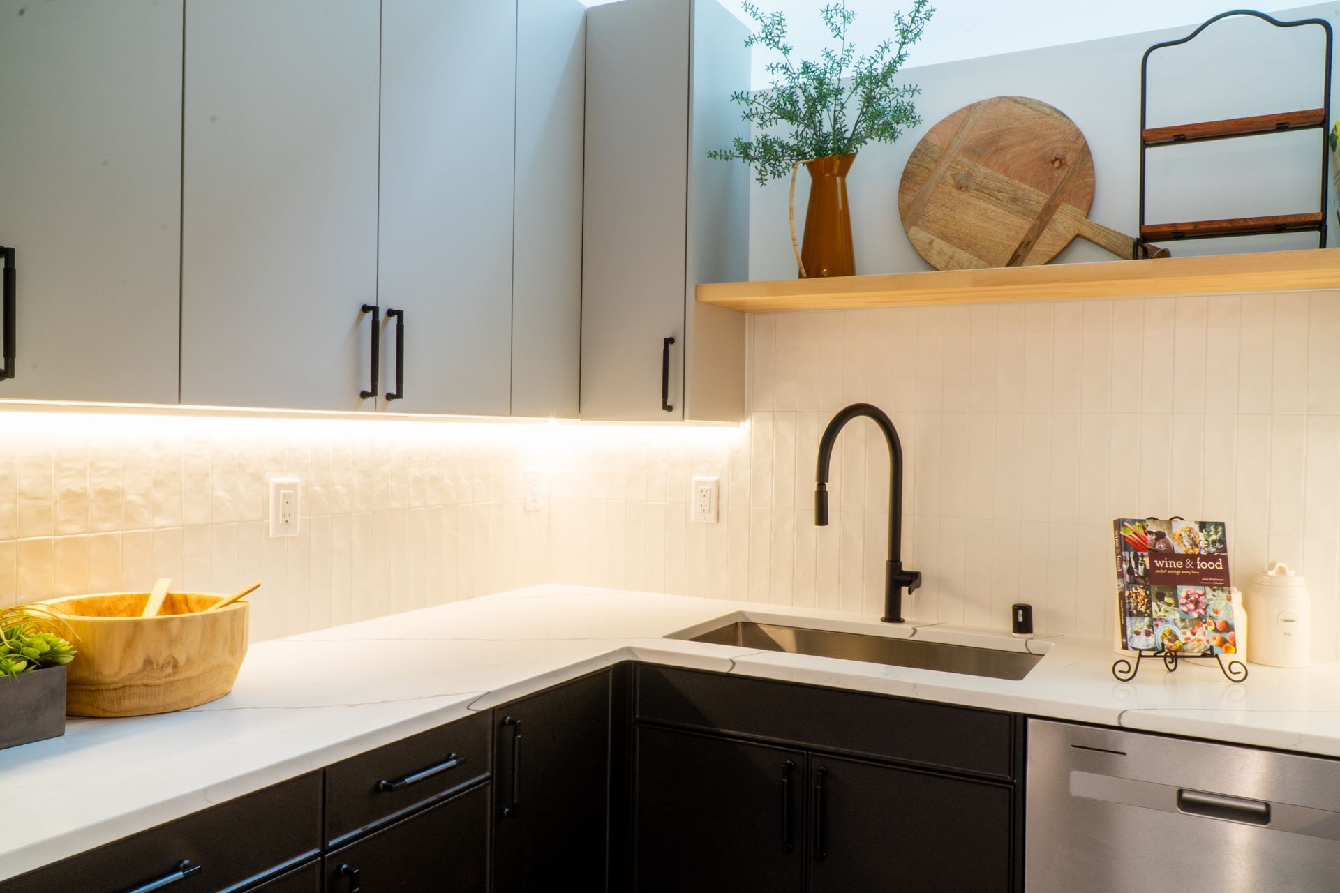 Modern kitchen with white cabinets, black lower cabinets, wood shelves, and a black faucet over a sink.