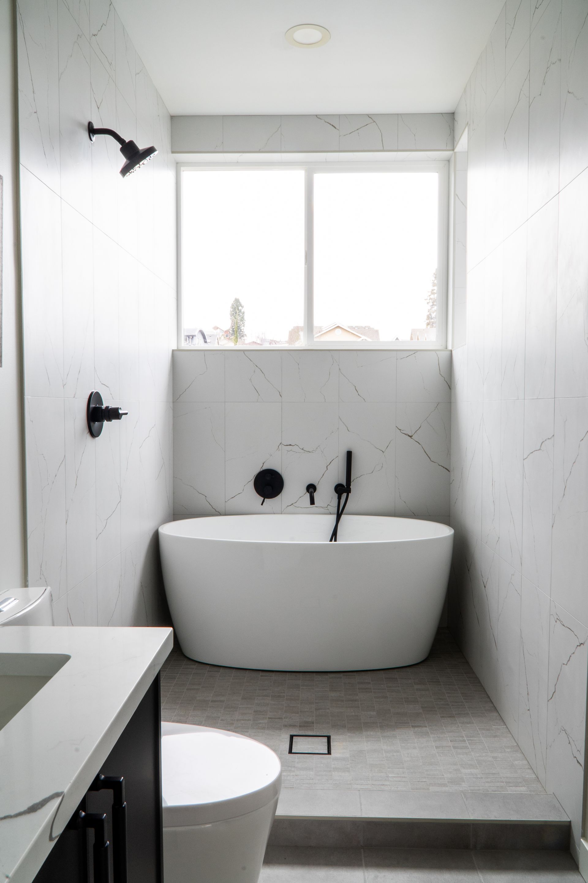 Minimalist white bathroom with a freestanding tub, showerhead, and window above the tub.