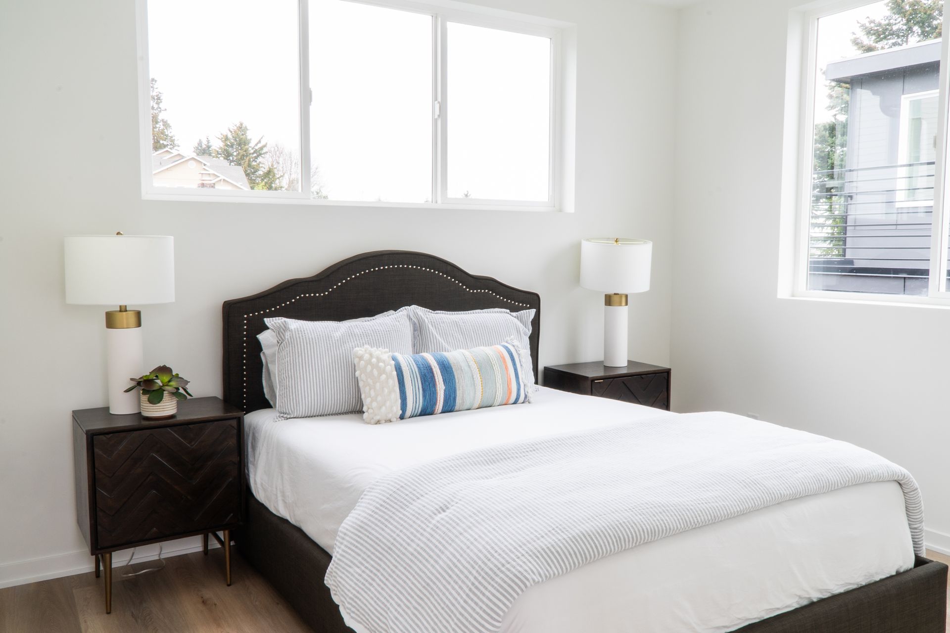 Modern bedroom with a dark bed, white bedding, and two bedside lamps by bright windows