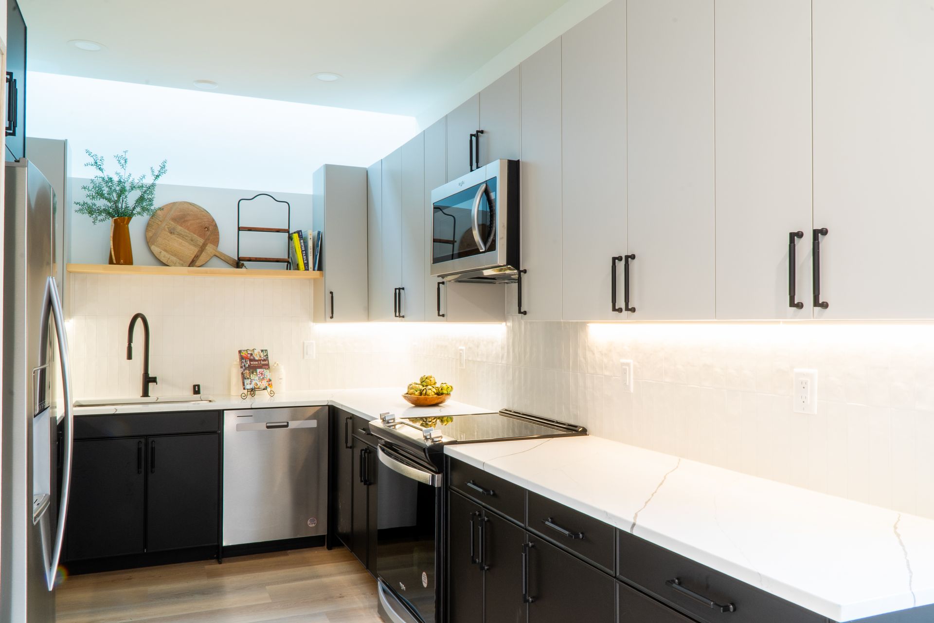 Modern kitchen with light wood cabinets, black lower cabinets, white countertops, and stainless steel appliances