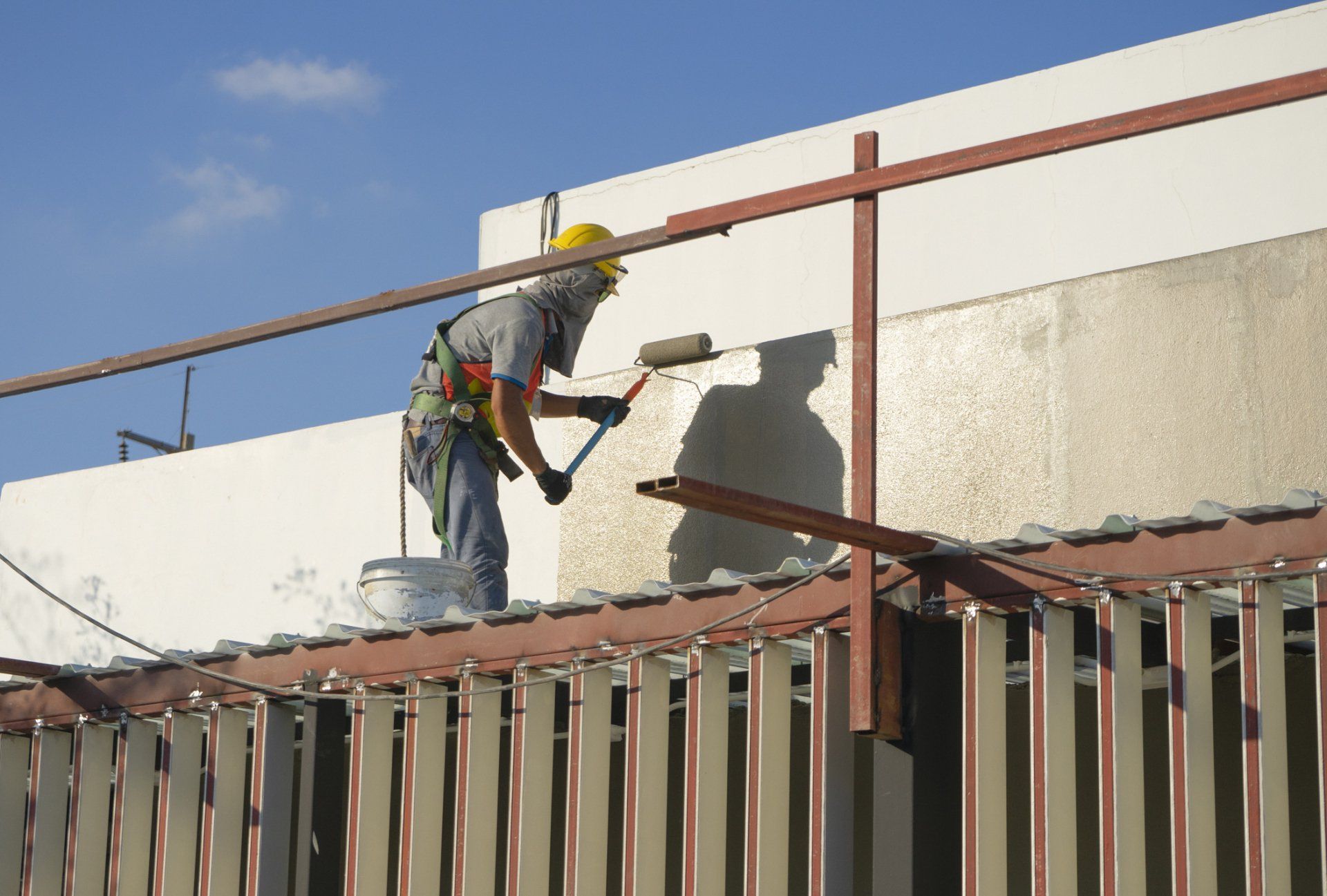 Worker painting a building wall from scaffolding under a blue sky