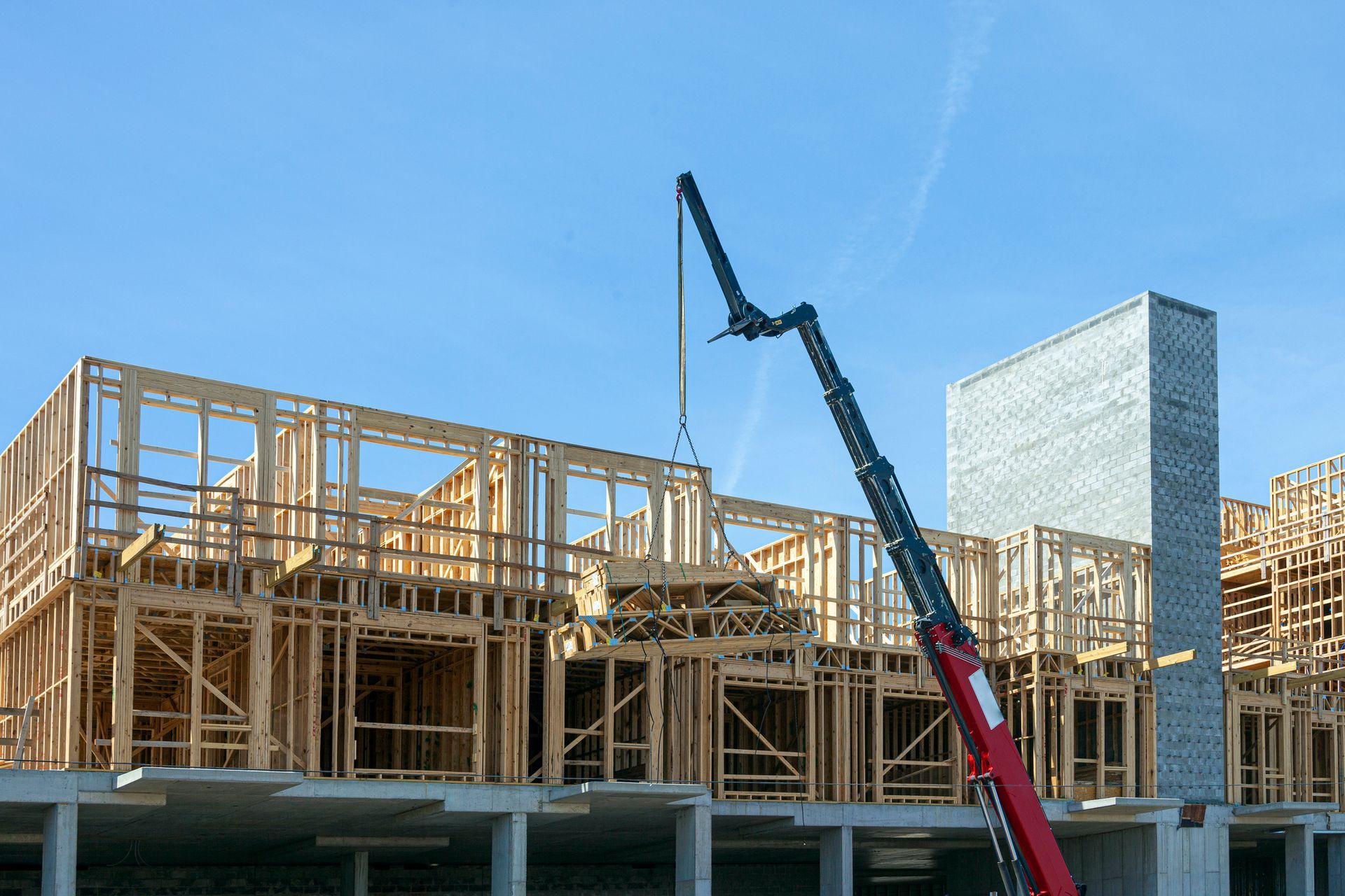 A crane is lifting a piece of wood on top of a building under construction.