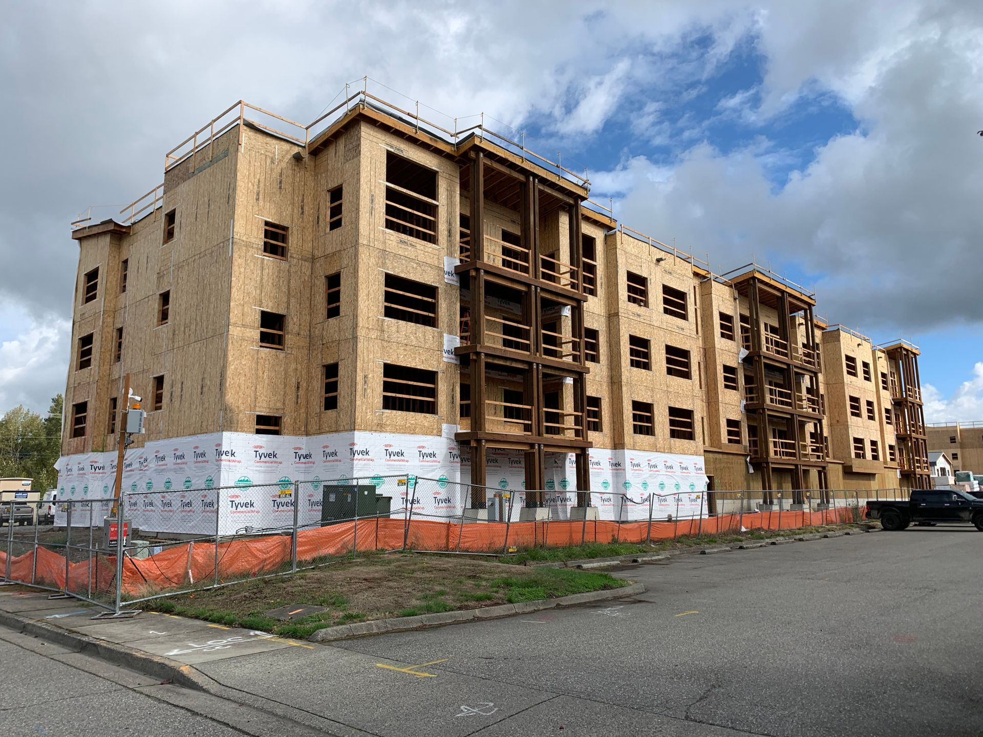 Partially built tan apartment complex with scaffolding and orange safety fencing along a street