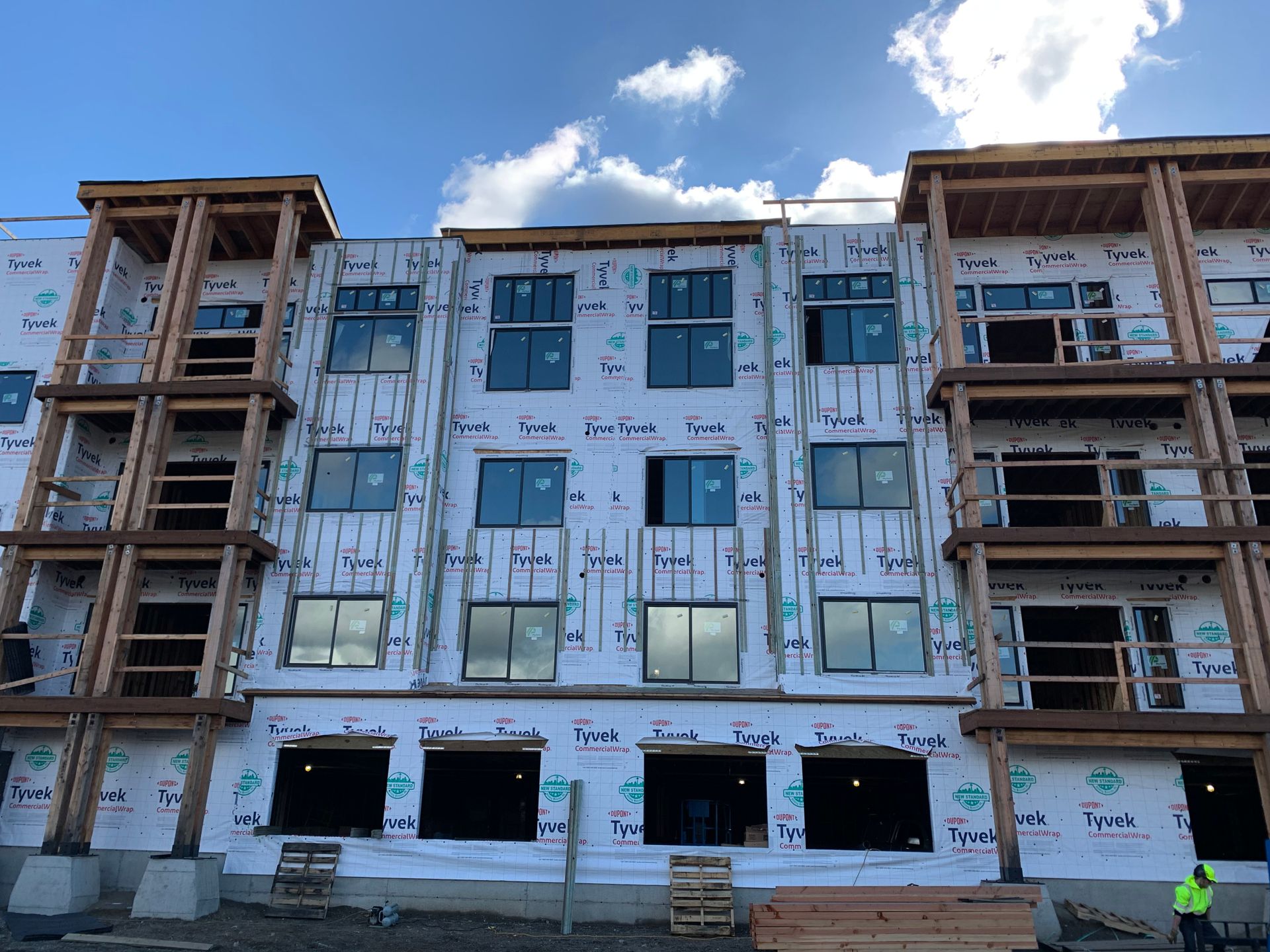 Partially built apartment building with exposed framing and white sheathing under a blue sky