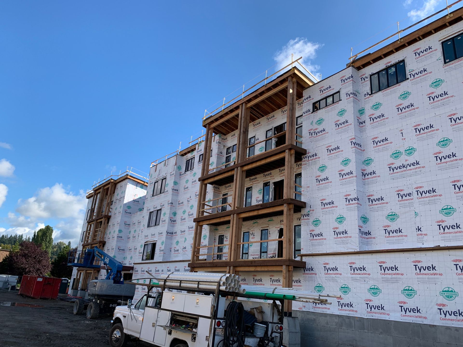 Apartment building under construction with white wrapped exterior and exposed wood framing under a blue sky