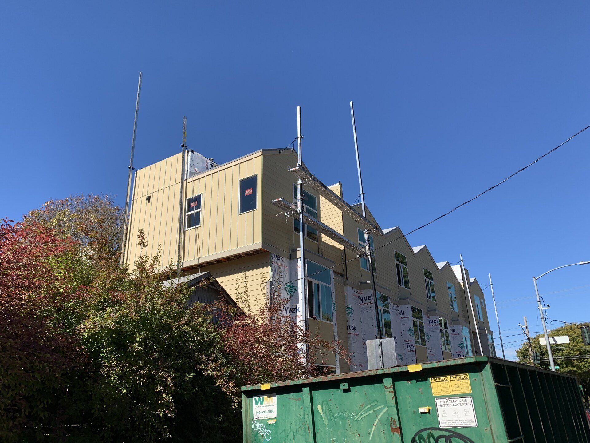 Low-rise beige building beside green dumpsters under a clear blue sky