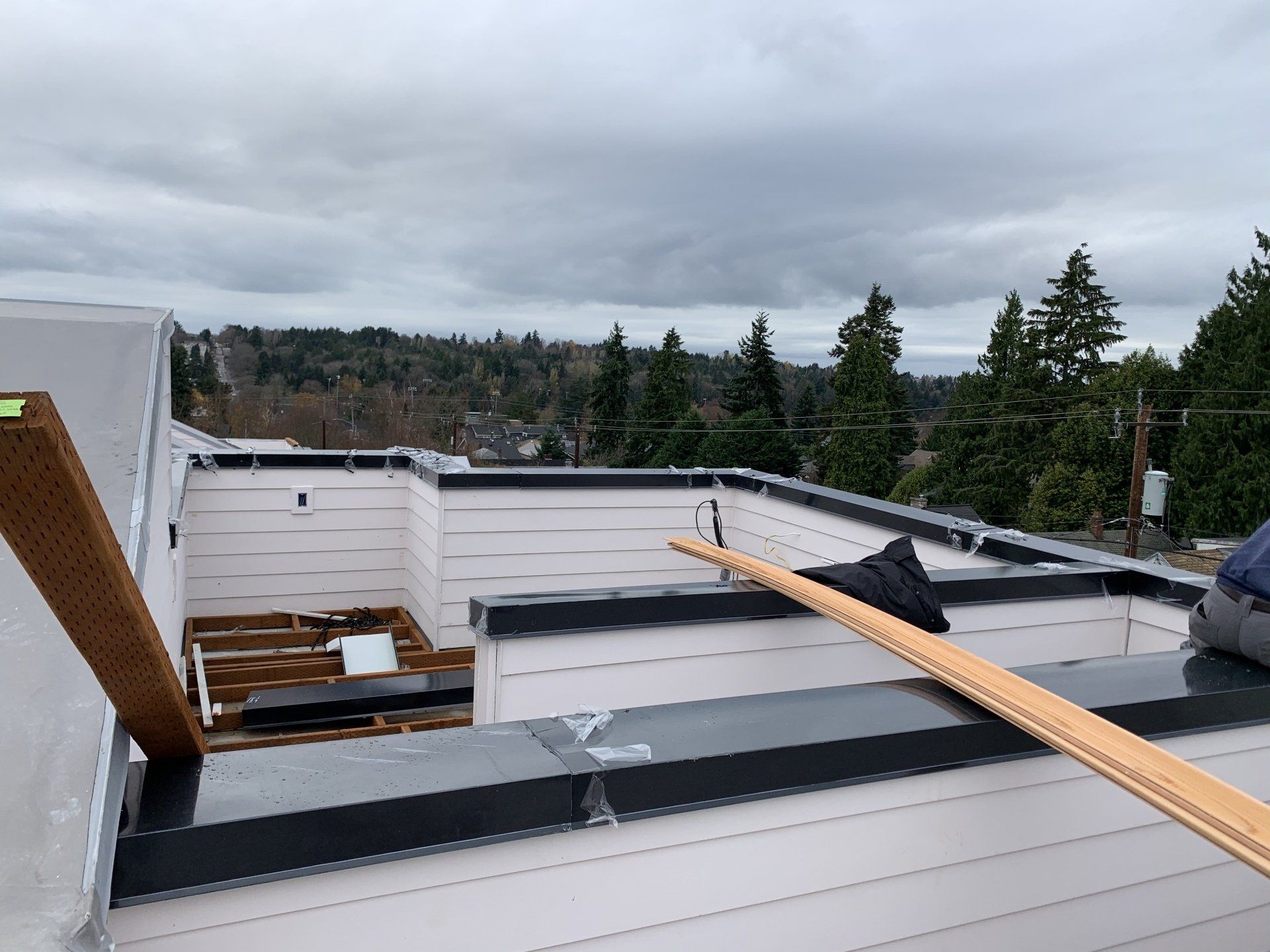 Rooftop construction site with white walls, wooden beams, and a cloudy sky over trees.