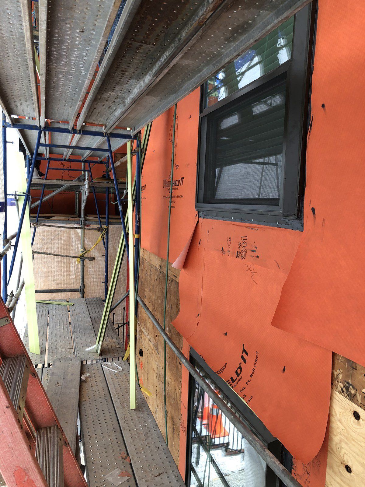 Scaffolding beside an orange building with windows and construction materials along a narrow walkway
