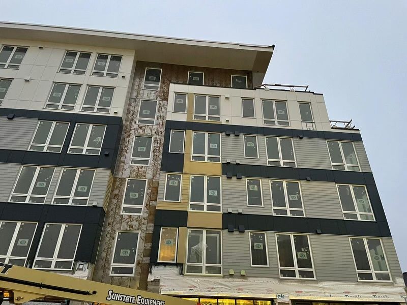 Modern multi-story apartment building with gray, black, and yellow exterior panels under a cloudy sky