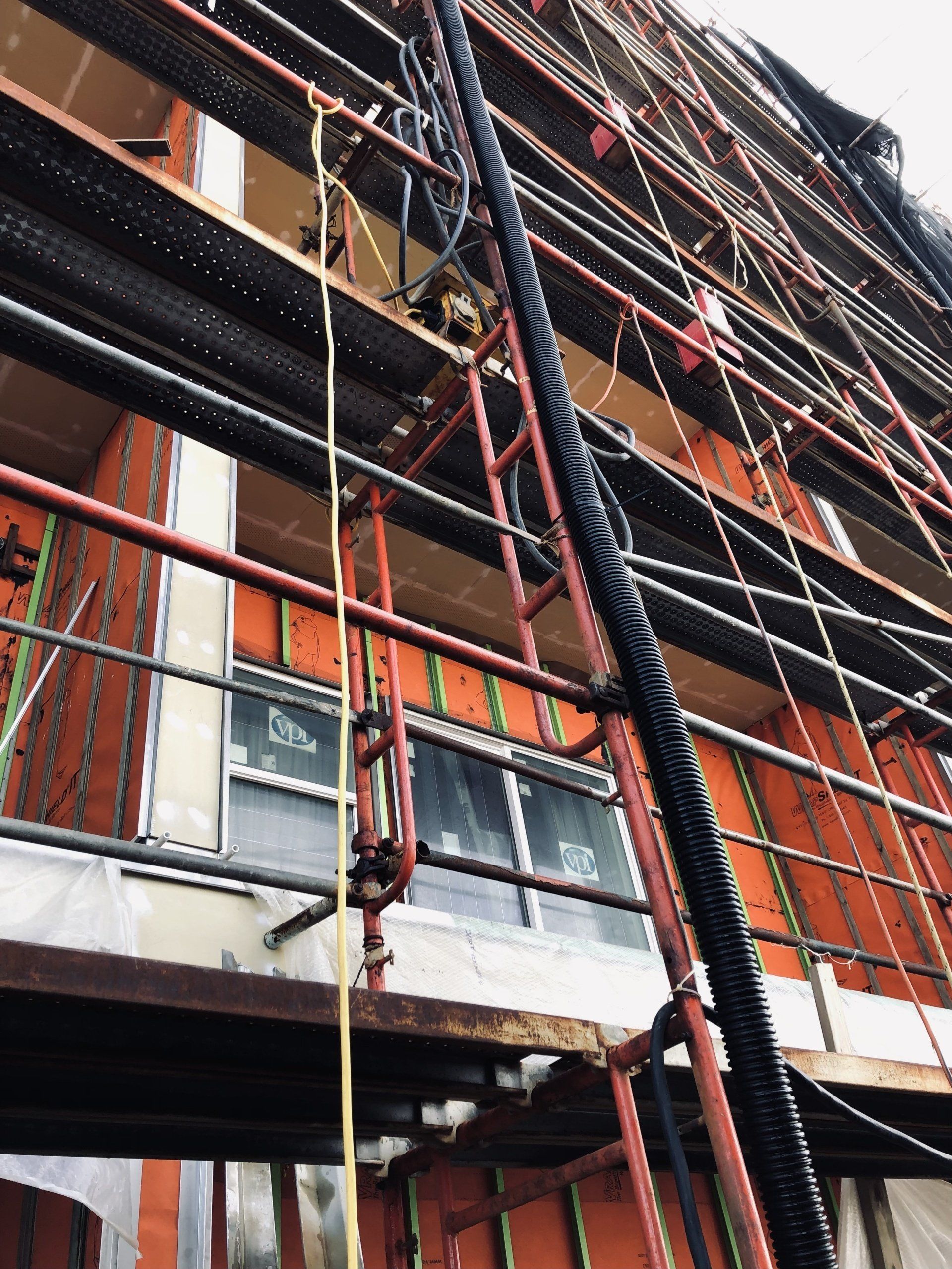 Brick building facade with scaffolding, hanging ropes, and construction materials on multiple floors