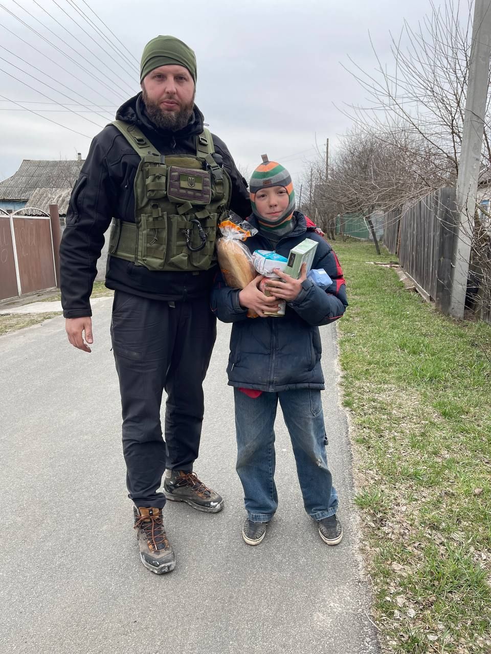 A man in a vest is standing next to a boy holding a bag of food.