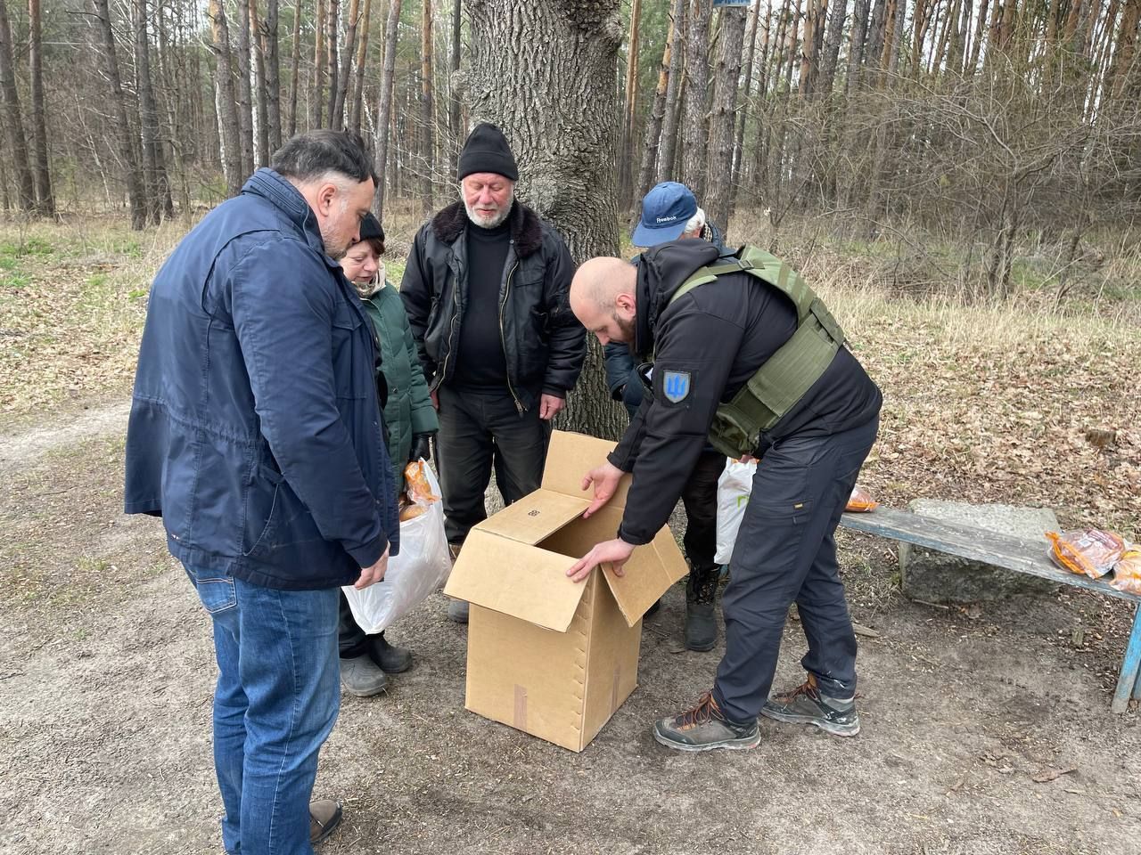 A group of men are standing around a cardboard box in the woods.