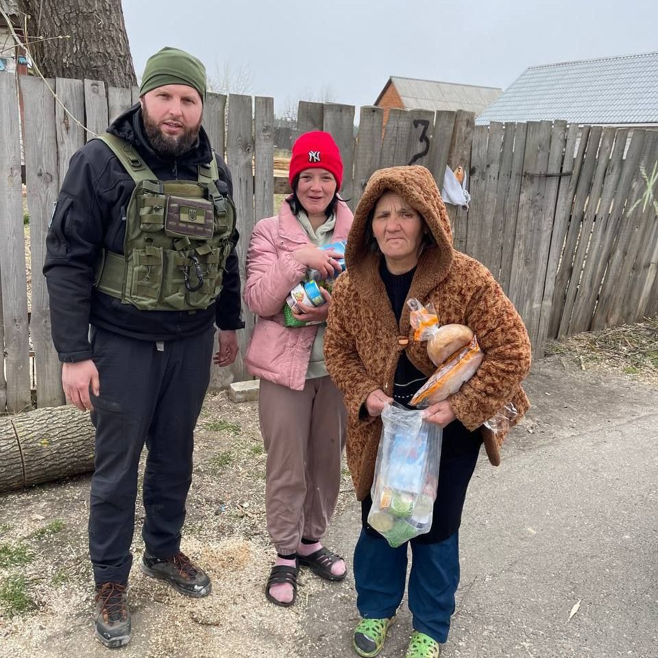 A man and two women are standing next to each other in front of a wooden fence.