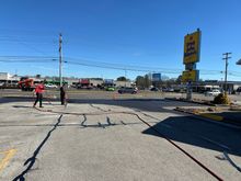 People walking across a cracked parking lot under a blue sky, with a tall yellow roadside sign nearby.