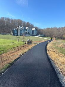 Curved black walkway leading to a white house on a grassy hill under a clear blue sky