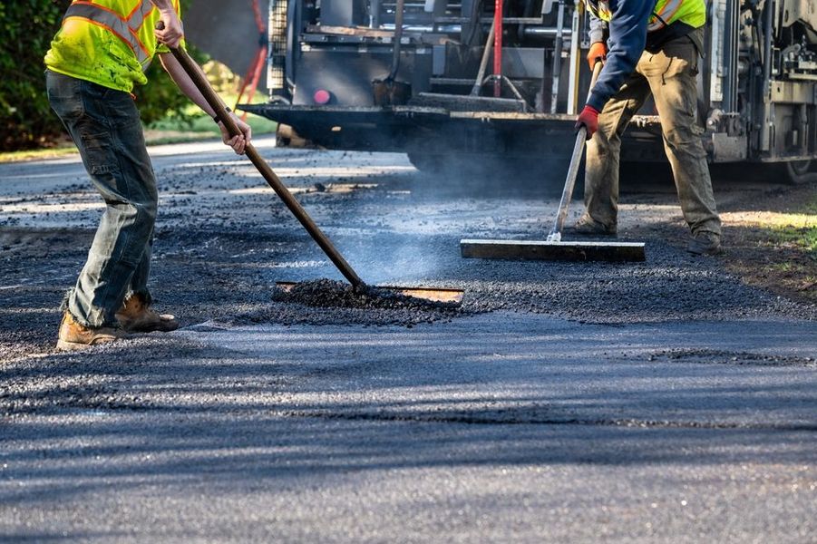 Workers spreading fresh asphalt on a road with shovels and rakes