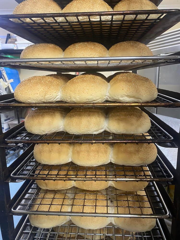 A Bunch Of Hamburger Buns Are Sitting On A Rack In A Bakery — Cedar Park Bakehouse in Taranganba, QLD
