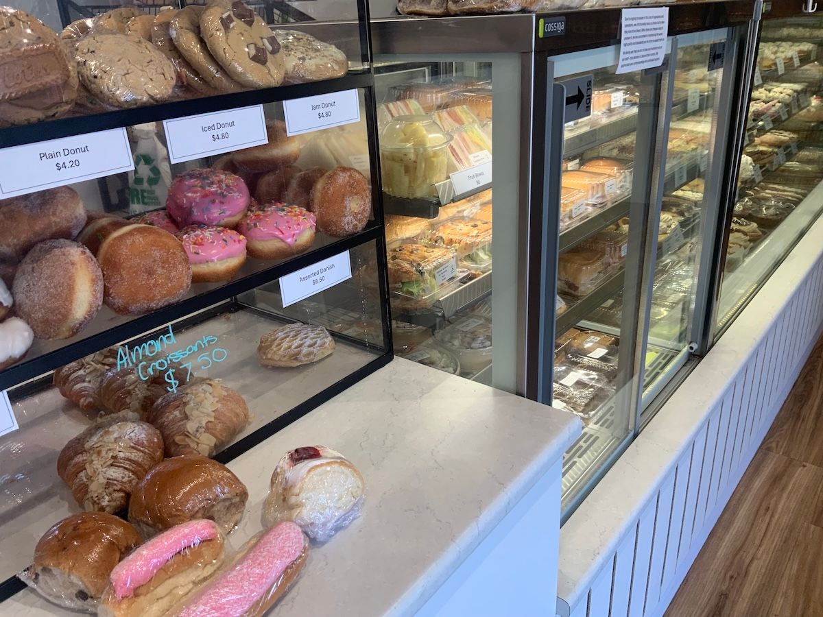 Bakery display case with assorted donuts, pastries, and breads on shelves and trays — Cedar Park Bakehouse in Taranganba, QLD