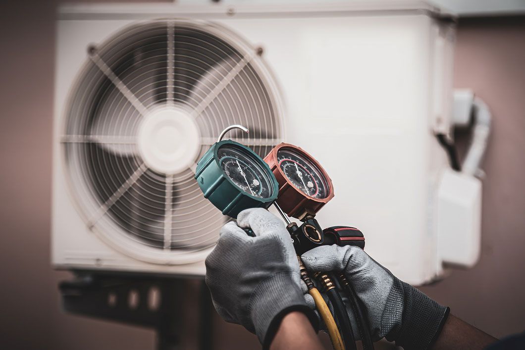 HVAC technician checking AC unit with gauges. White unit outside. Hands wear gloves.