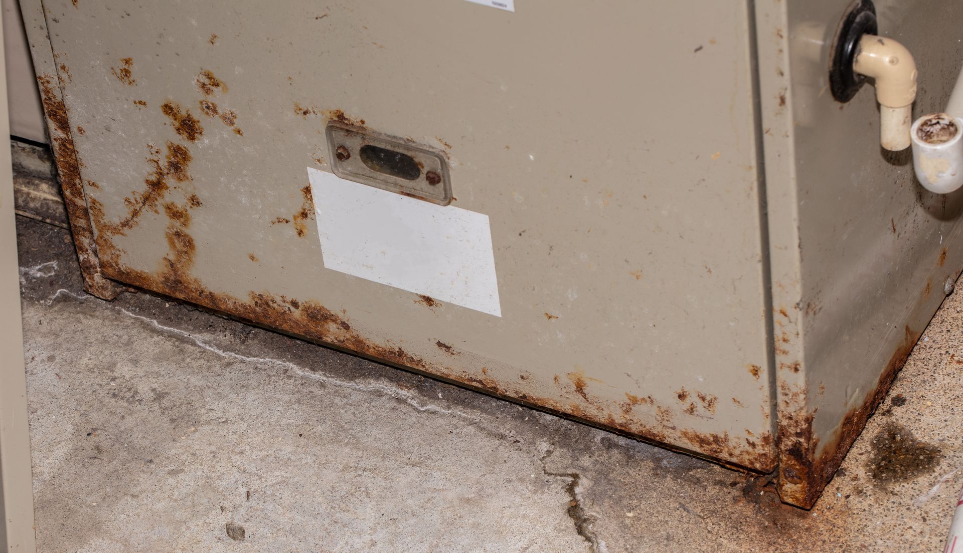 Rusty beige HVAC unit with rust stains along the bottom edges and side near concrete floor Rusty beige HVAC unit with rust stains along the bottom edges and side near concrete floor